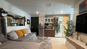 A modern living room with a sofa, a coffee table, and a TV. There is a kitchen area with cabinets and a refrigerator. - Elegant Tranquil Restful Oasis with Pure Serenity Pool and Garden Suite Studio (Miami)