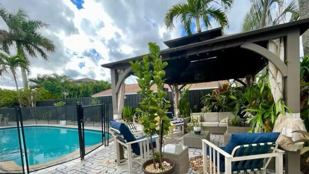 A poolside area with a covered seating area, a potted plant, and a pool. - Elegant Tranquil Restful Oasis with Pure Serenity Pool and Garden Suite Studio (Miami)