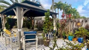 A covered outdoor seating area with lounge chairs and a pergola, surrounded by potted plants and palm trees. - Elegant Tranquil Restful Oasis with Pure Serenity Pool and Garden Suite Studio (Miami)