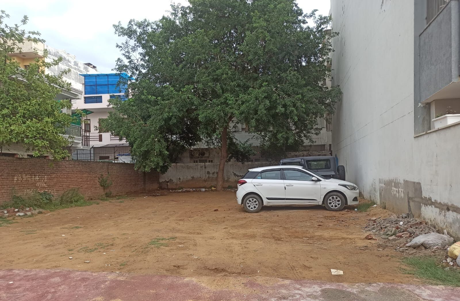 A white car parked in a dirt area with a tree and a building in the background.