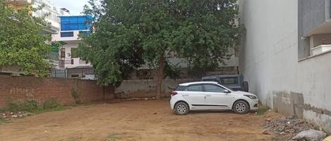 A white car parked in a dirt area with a tree and a building in the background.