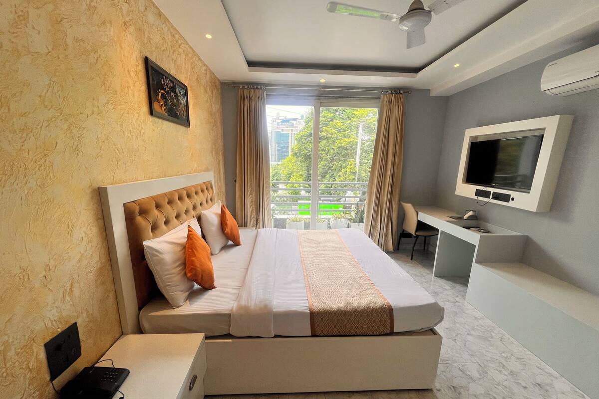 Una habitación de hotel moderna con una cama grande, un escritorio, un televisor y un balcón con vistas a zonas verdes.