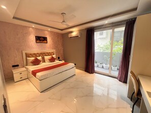 A modern bedroom with a large bed, a ceiling fan, and a view of a balcony with potted plants. - Hotel VS Residency Medanta (Gurugram)