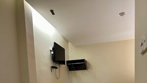 Habitació d'hotel amb un llit, una televisió penjada a la paret, una petita estant, una tetera i una safata amb tasses i una ampolla.
