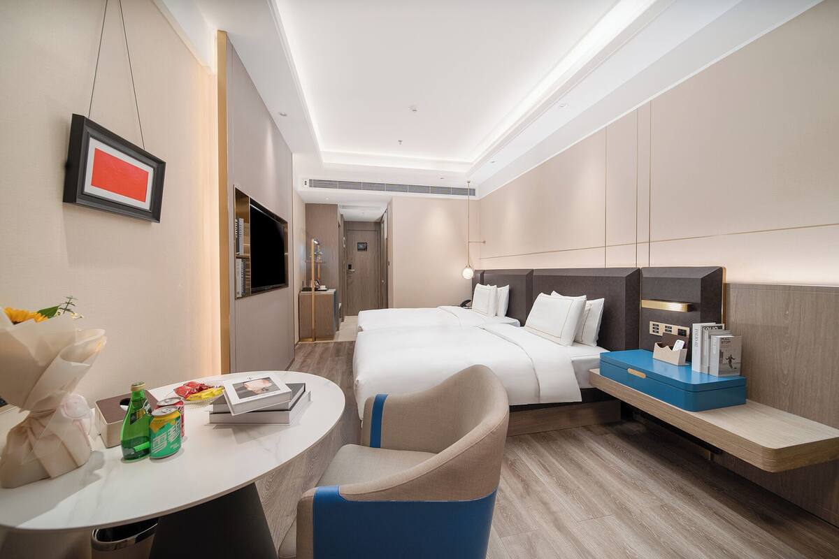 Quarto de hotel com cama, escrivaninha, cadeira, televisão e minibar.
