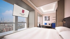 A hotel room with a large bed, a desk, a chair, a small table with a vase, and a city view. - Echarm plus International Hotel Guangzhou Changgang Subway Station - Free Shuttle Bus to Canton Fair Complex During Canton Fair Period (Guangzhou)