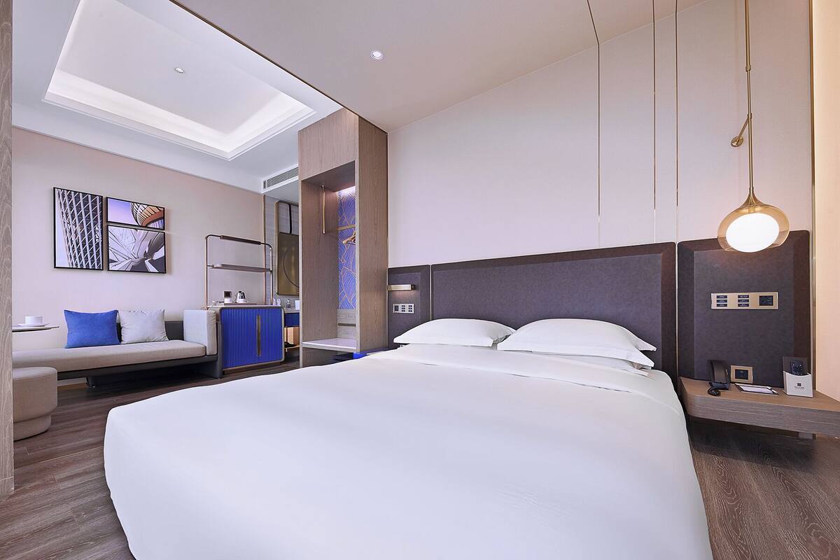 Quarto de hotel moderno com uma cama grande, um sofá, uma escrivaninha e um claraboia.
