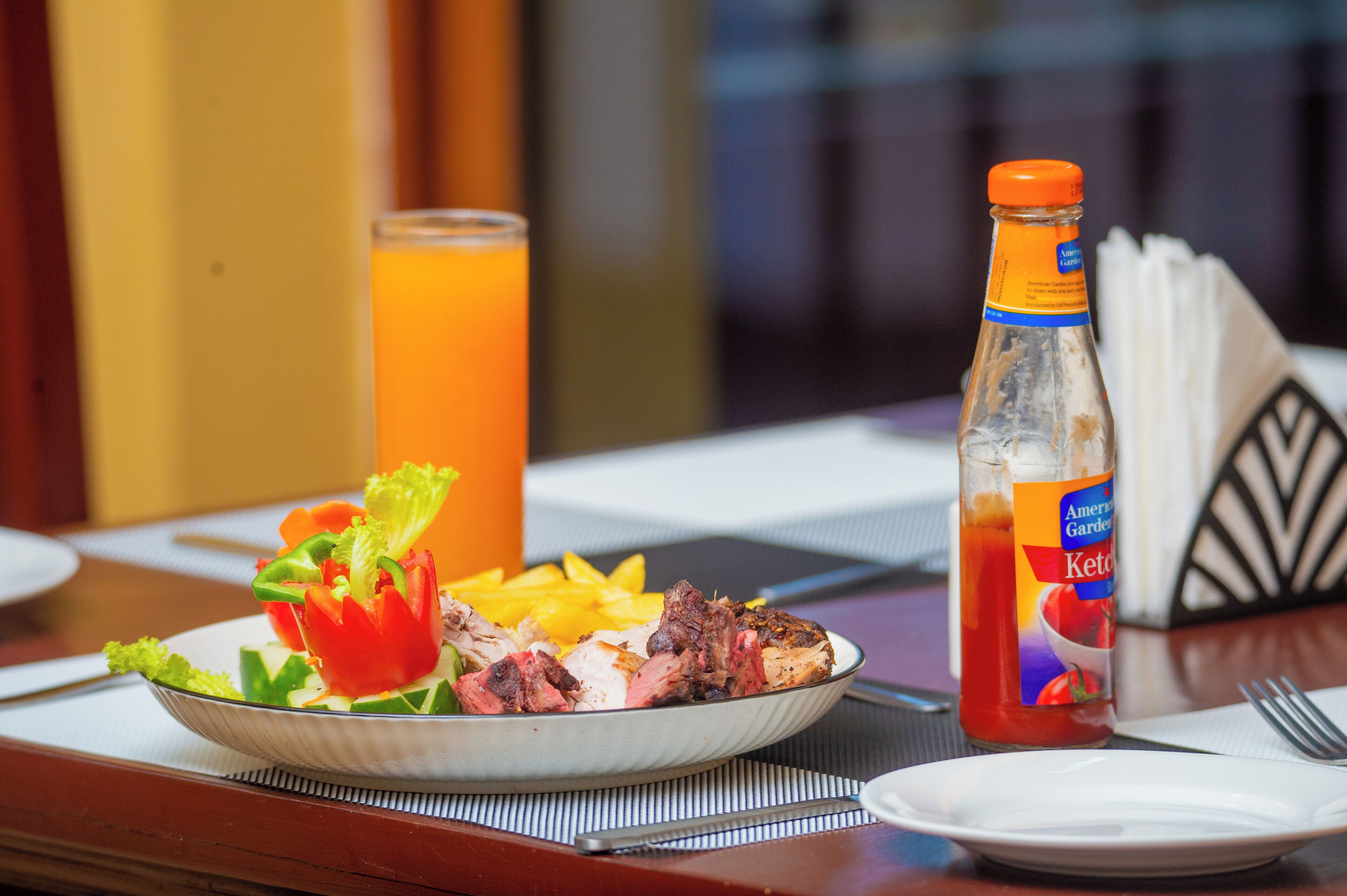 A breakfast plate with steak, fries, and salad, a glass of orange juice, and a bottle of ketchup.