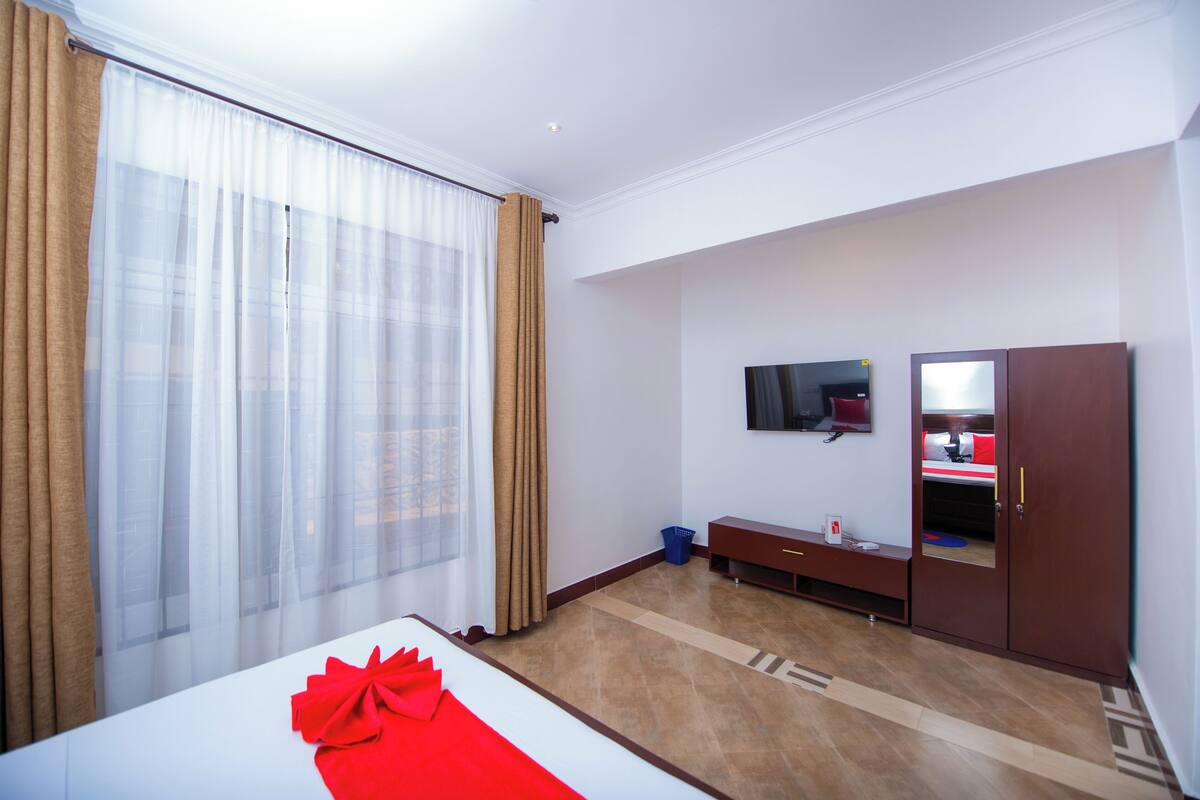 A hotel room with a bed, a TV, a wardrobe, and a window with curtains.
