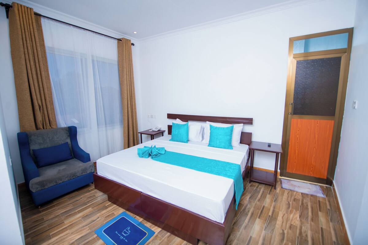 A hotel room with a bed, a sofa, a nightstand, and a wooden floor.