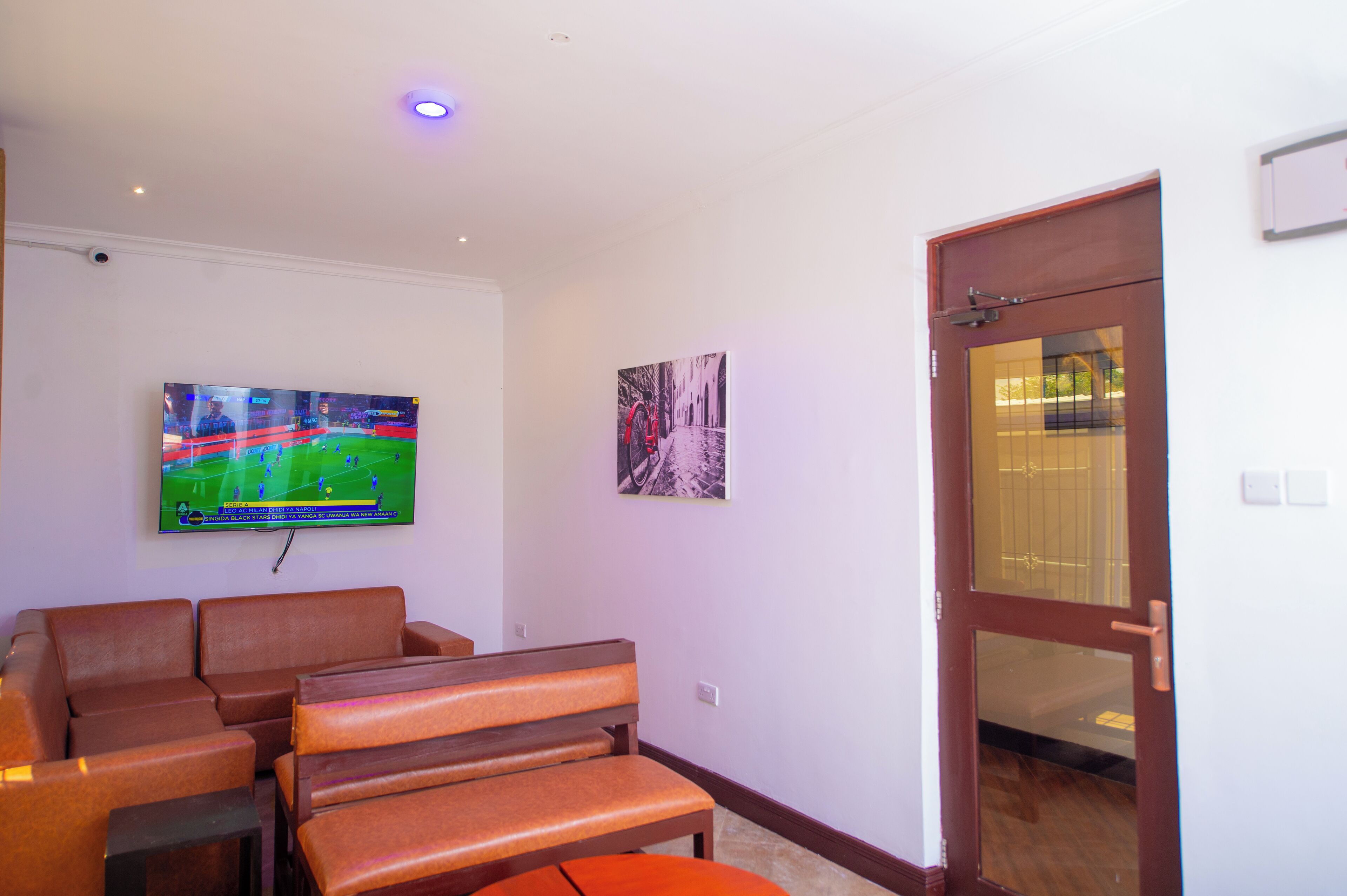 A living room with a flat-screen TV, a bench, a door, and a wall-mounted picture.
