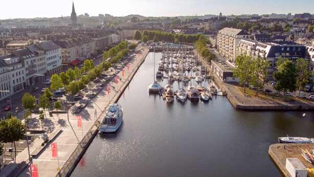 Una marina con barcos amarrados a lo largo de un canal, rodeada de edificios y árboles.