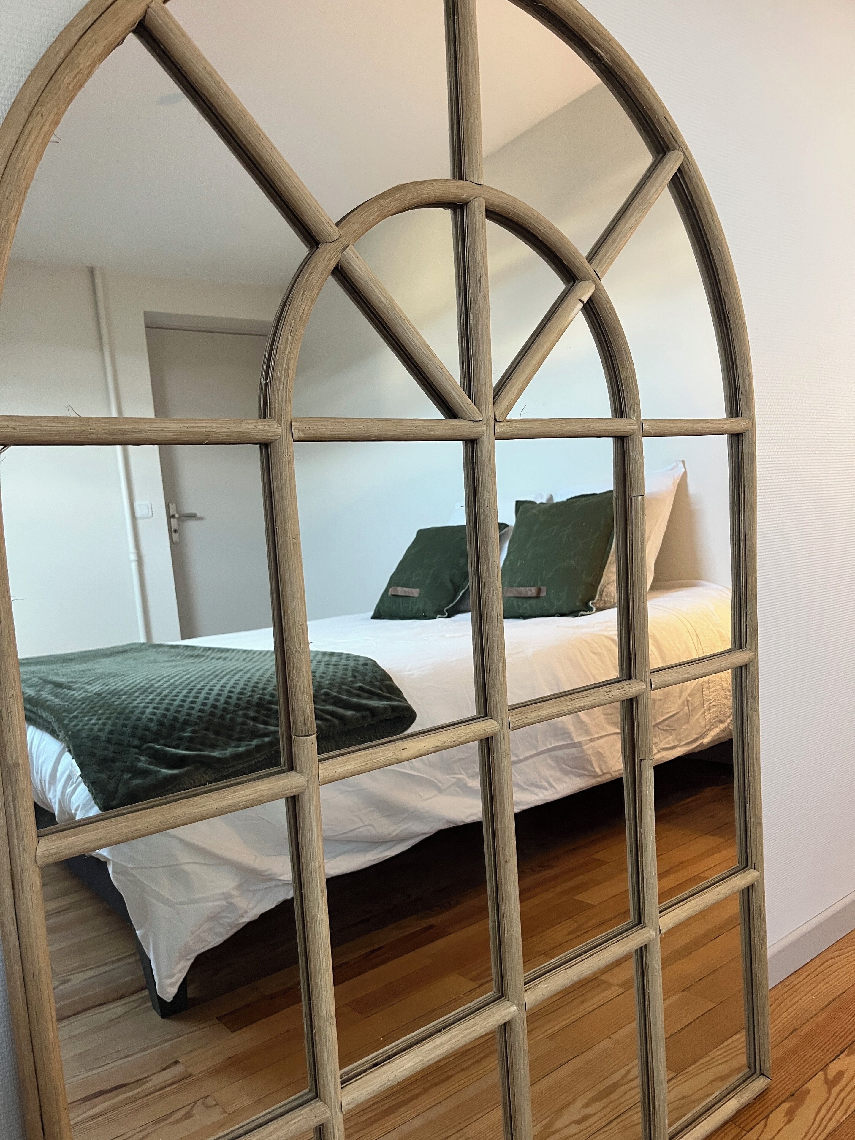 Een kamer met een bed, een spiegel met houten lijst en een deur.