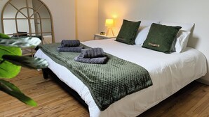Una cama bien hecha con una manta y almohadas verdes, una lámpara de noche y suelo de madera.
