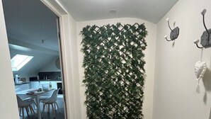 Una habitación pequeña y acogedora con un banco blanco, una pared decorada de verde, una pequeña mesa con sillas y un tragaluz al fondo.