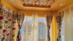 A room with wooden ceiling and yellow walls, featuring a large window with white curtains and a door. - Oak Heaven Cottage (Baramula)