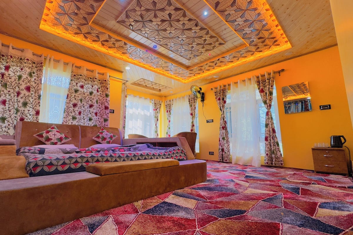 Un dormitorio con alfombra estampada, una cama con almohadas florales y un techo con diseños intrincados.