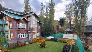 A multi-story building with a brick facade and green roof, surrounded by a well-maintained garden with various flower beds and a lawn. - Oak Heaven Cottage (Baramula)