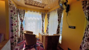 A room with a wooden ceiling, patterned curtains, a fan, and a chair. - Oak Heaven Cottage (Baramula)
