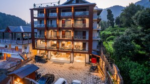 Un hotel de varios pisos con un diseño moderno, que cuenta con balcones en cada planta, un patio central y un telón de fondo montañoso.