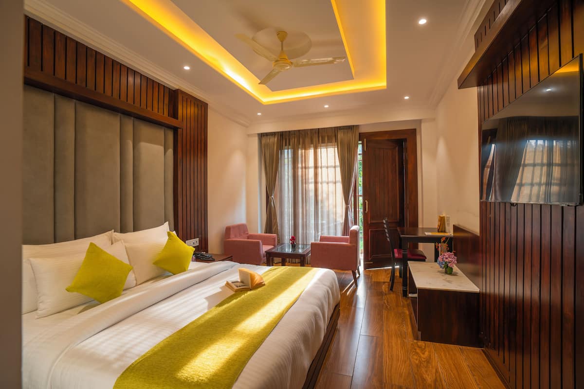 A hotel room with a large bed, a desk, two chairs, a TV, and a ceiling fan.