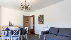 A dining area with a table set for four, a sofa, a chandelier, and a door leading to another room. - Les Voiles by Interhome (Six Fours)