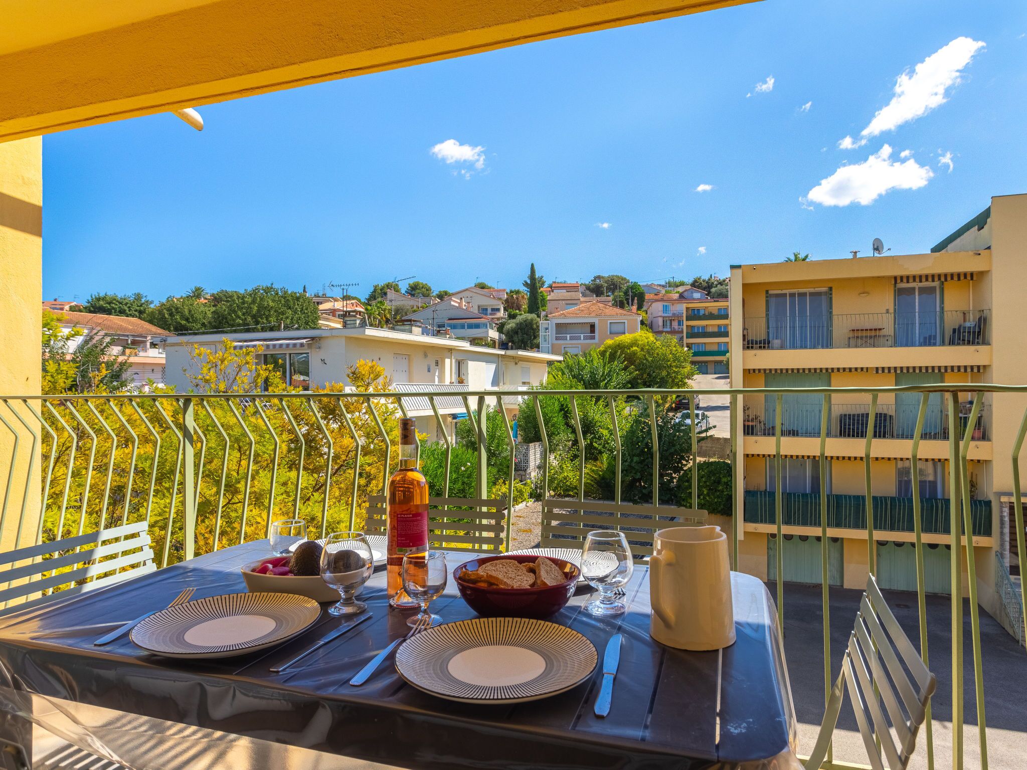 A balcony with a table set for two, overlooking a residential area with buildings and trees.