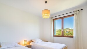 A bedroom with two beds, a nightstand, a lamp, a window with a view, and a chair. - Les Voiles by Interhome (Six Fours)