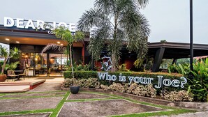 The exterior of a coffee shop named 'DEAR JOES' with a neon sign reading 'Who is your Joe?' and a well-maintained outdoor seating area. - Precious Florannjoe Chic New Studio With Best Care (Las Pinas)