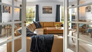 A spacious living room with a large sectional sofa, a coffee table, and a view through glass doors to an outdoor area.