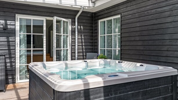 A hot tub in a covered outdoor area with wooden walls and glass doors.