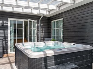 Een hottub in een overdekte buitenruimte met houten wanden en glazen deuren.