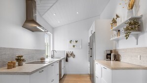A modern kitchen with white cabinetry, a wooden floor, and a stainless steel range hood.