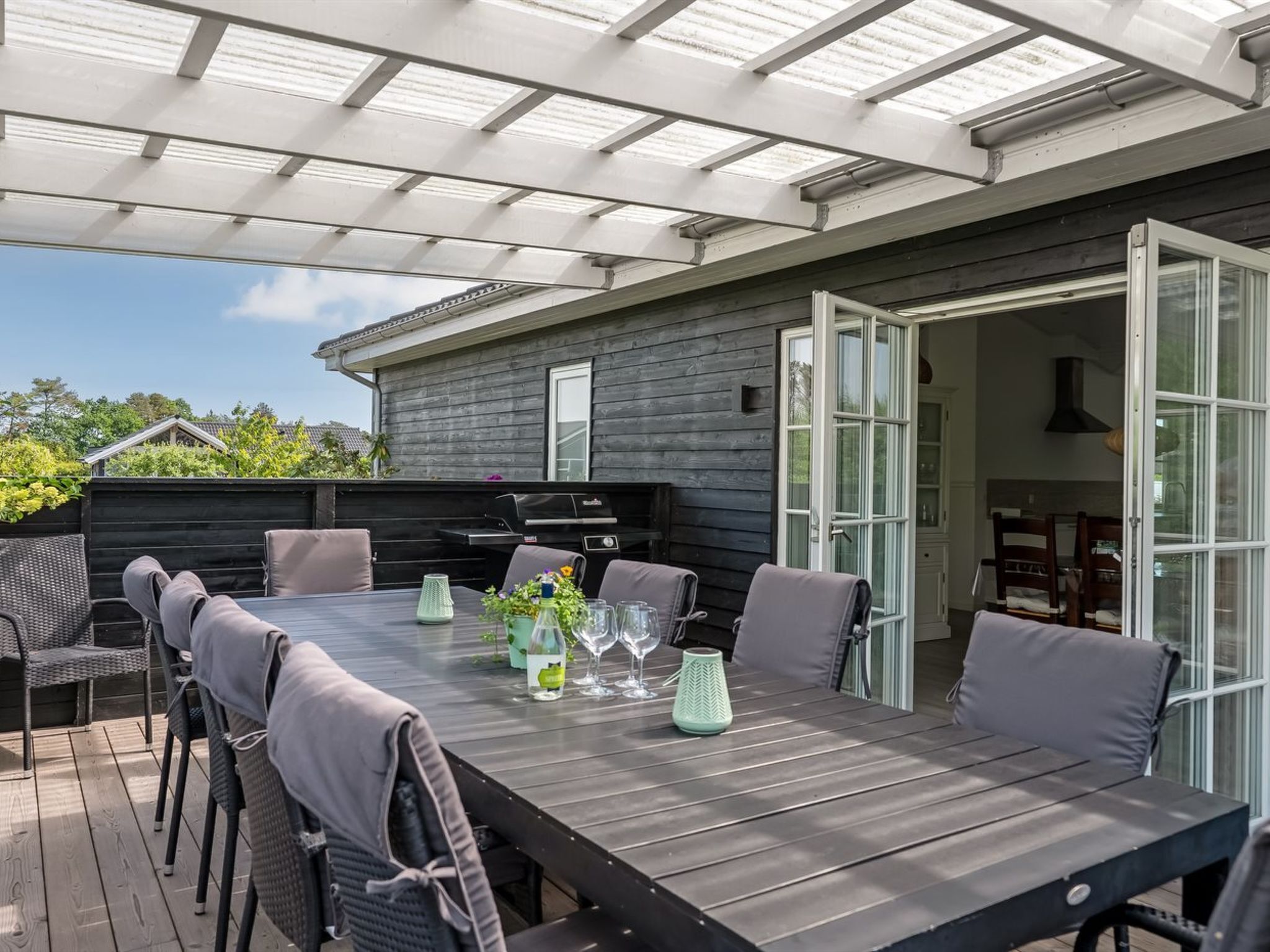 Een terras buiten met een lange tafel, stoelen en een barbecue.