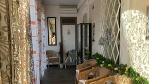 A hallway with wicker furniture, a clock, and patterned curtains. - Hotel Clair Logis (Argelès-sur-Mer)