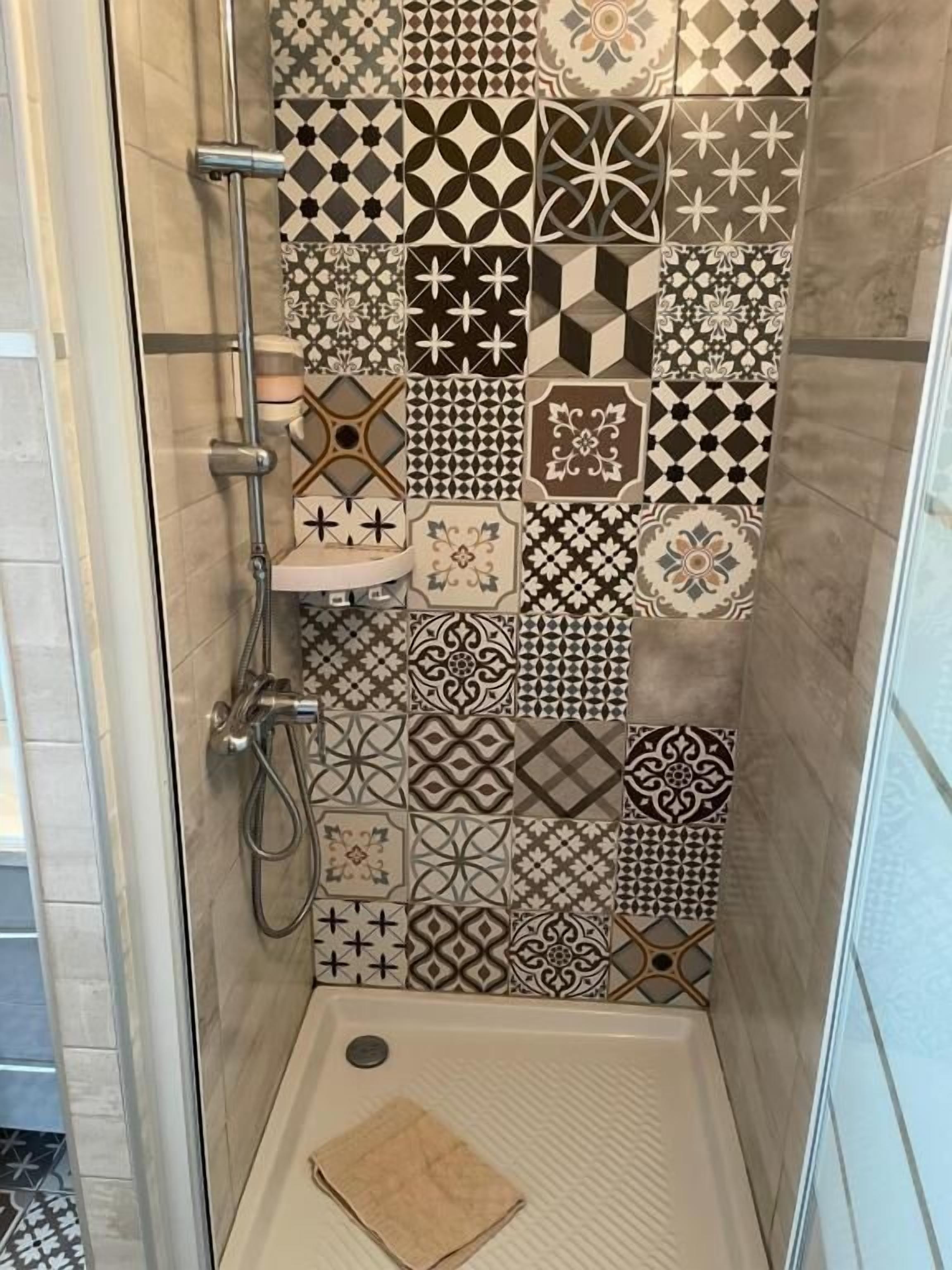 En dusch med en kaklad vägg som har en mängd olika geometriska och blommiga mönster.