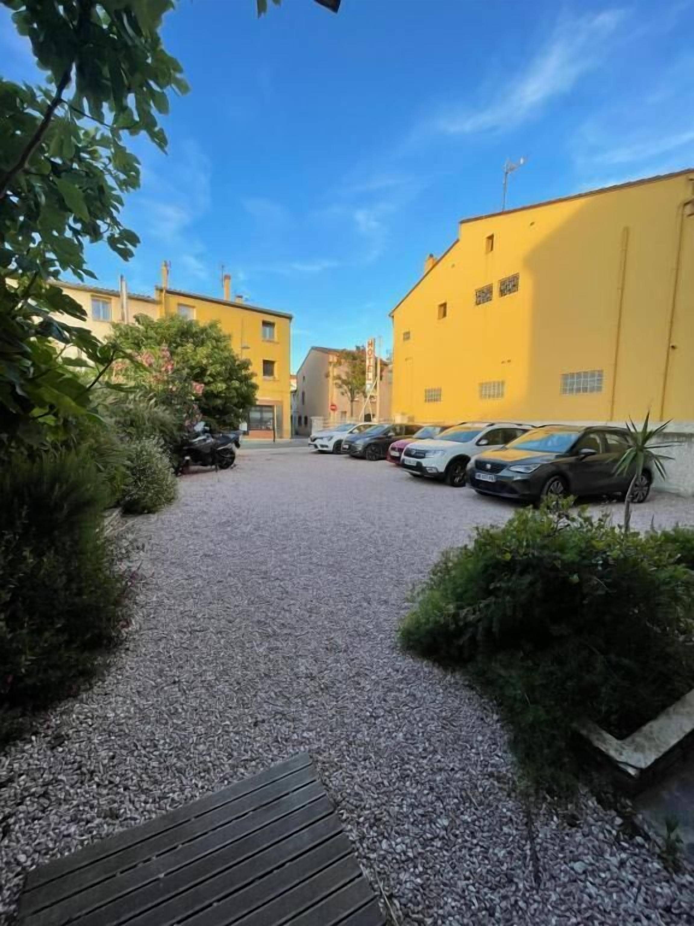 A parking area with several cars, a gravel path, and yellow buildings.