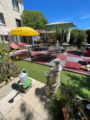 Une terrasse extérieure avec des tables et des chaises, des parasols et une statue.