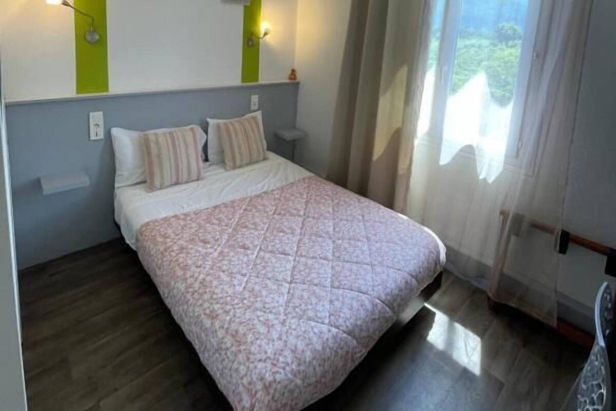 Un dormitorio con una cama, dos luces fijadas a la pared, una ventana con cortinas y vistas al exterior.