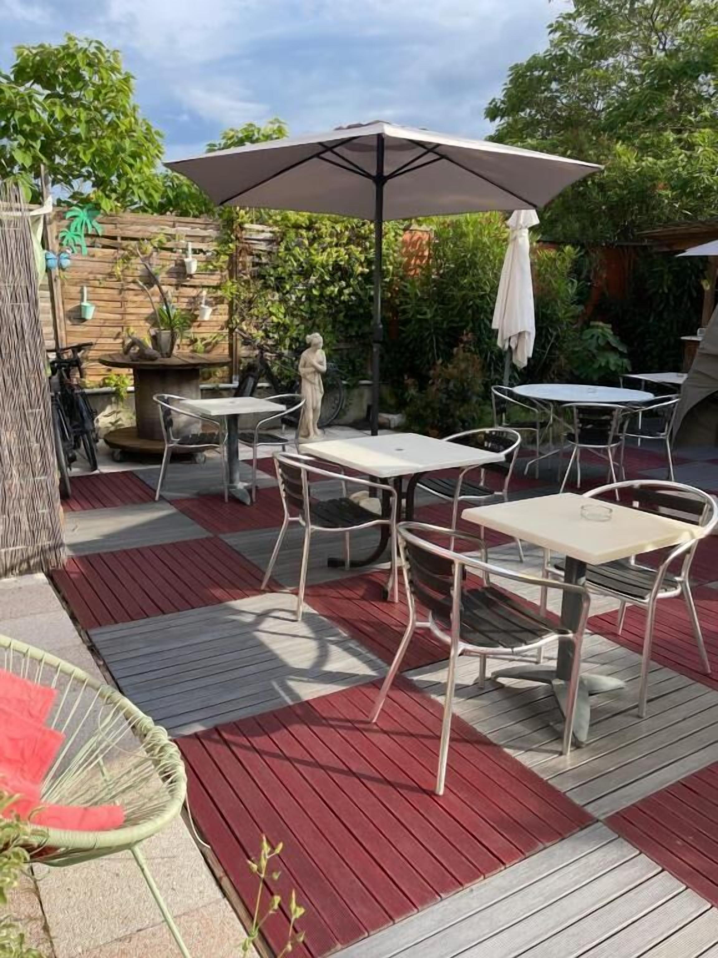 Une terrasse extérieure avec des tables et des chaises en métal, un grand parasol et un mur en pierre agrémenté de plantes en pot.