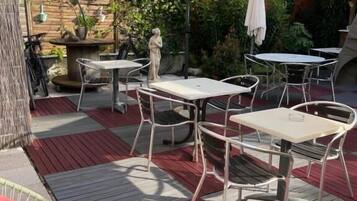 Une terrasse extérieure avec des tables et des chaises en métal, un grand parasol et un mur en pierre agrémenté de plantes en pot.