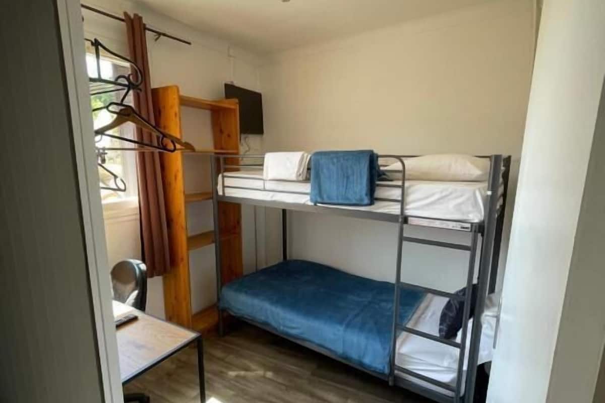 Una habitación pequeña y funcional con literas, un escritorio y una silla.