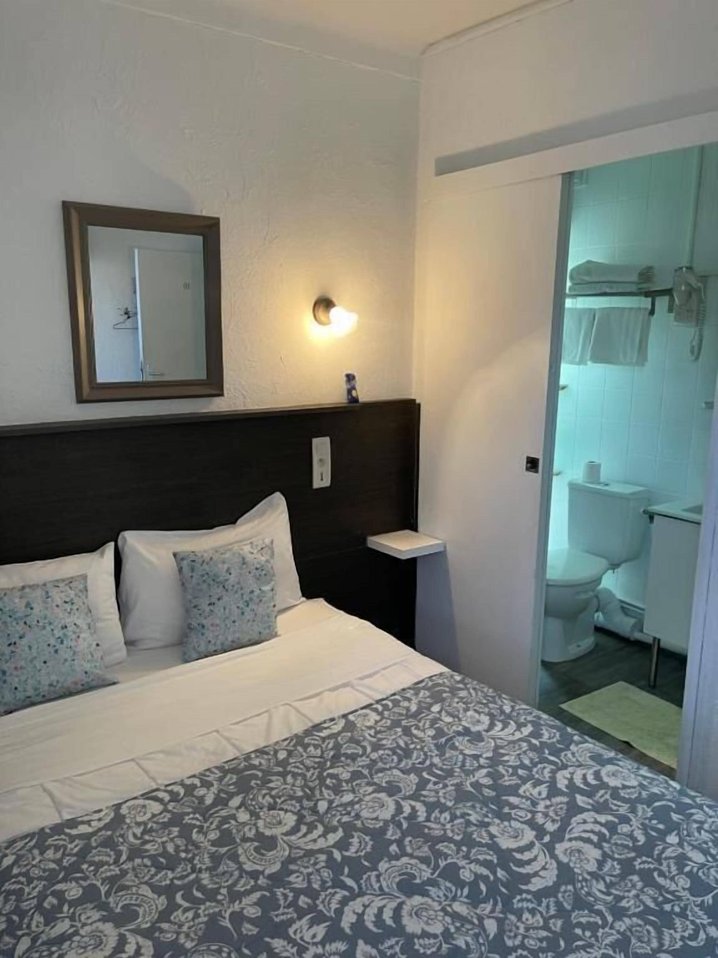 Een hotelkamer met een bed, nachtkastje, spiegel en een badkamer die door een open deur zichtbaar is.