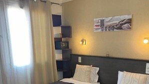 A hotel room with two beds, a bedside table, a lamp, a shelf with items, and a poster on the wall. - Hotel Clair Logis (Argelès-sur-Mer)