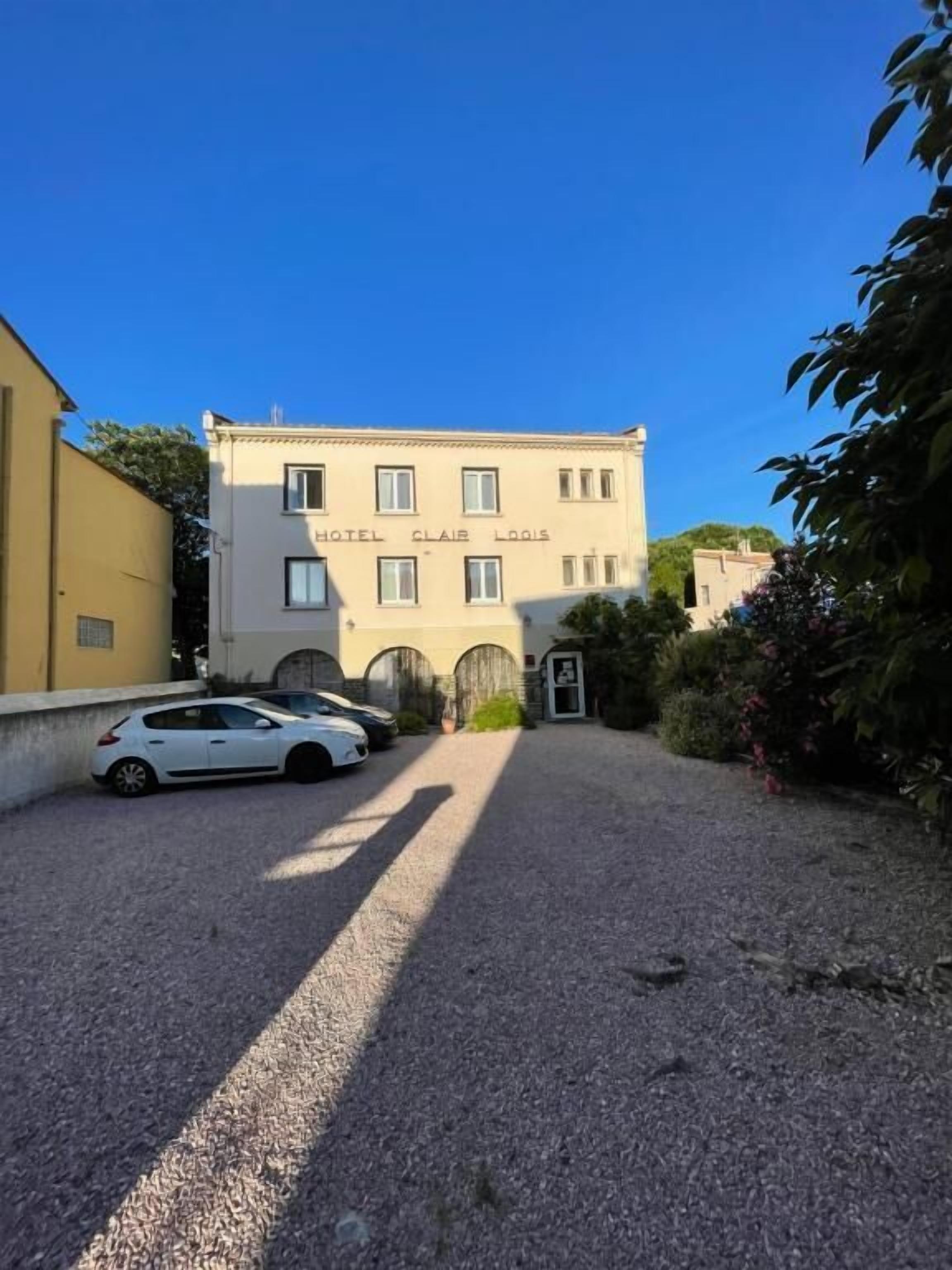 A building labeled "HOTEL CLAIR LOGIS" with a gravel driveway and parked cars.