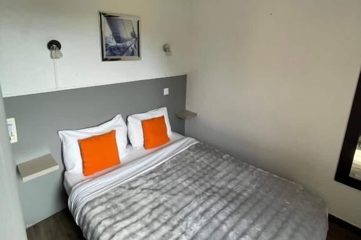 Un dormitorio con una cama, dos almohadas, una mesita de noche, una lámpara de pared y un cuadro enmarcado.