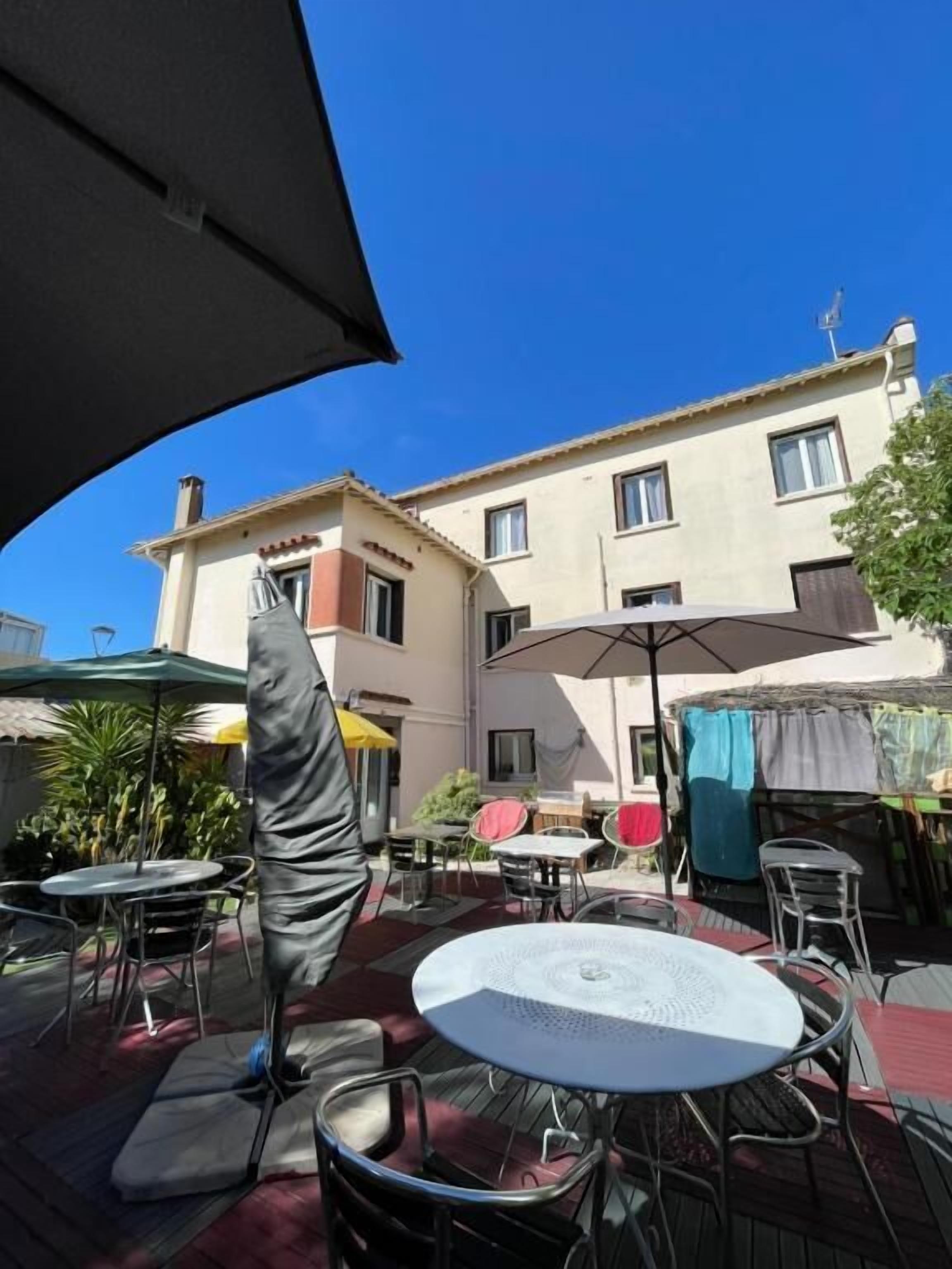 An outdoor patio area with round tables and chairs, umbrellas, and a building in the background.