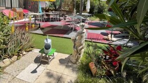 An outdoor patio area with tables and chairs, umbrellas, and a statue. - Hotel Clair Logis (Argelès-sur-Mer)