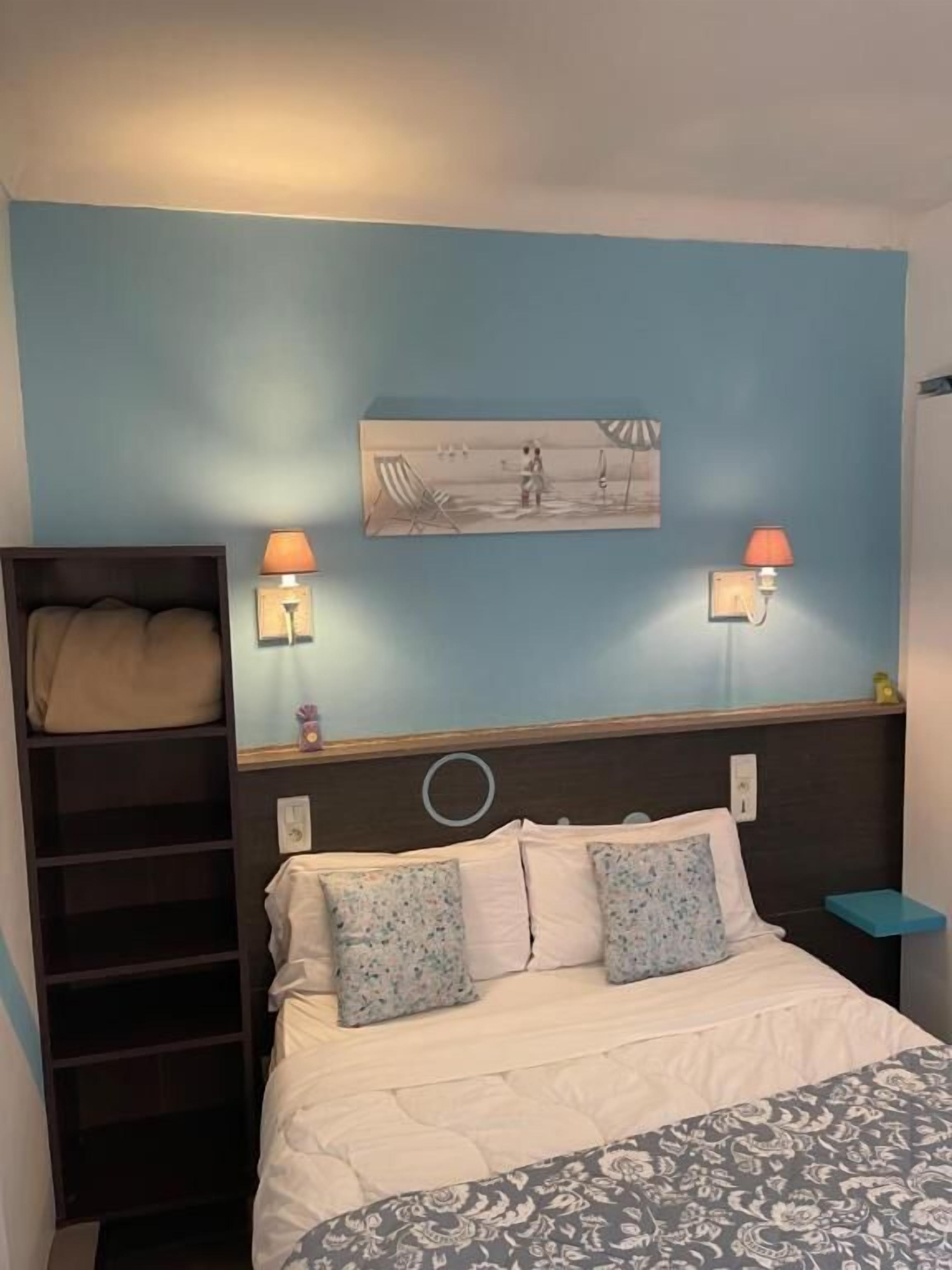 A bedroom with a bed, a nightstand, a shelf with a lamp, and a wall-mounted picture.