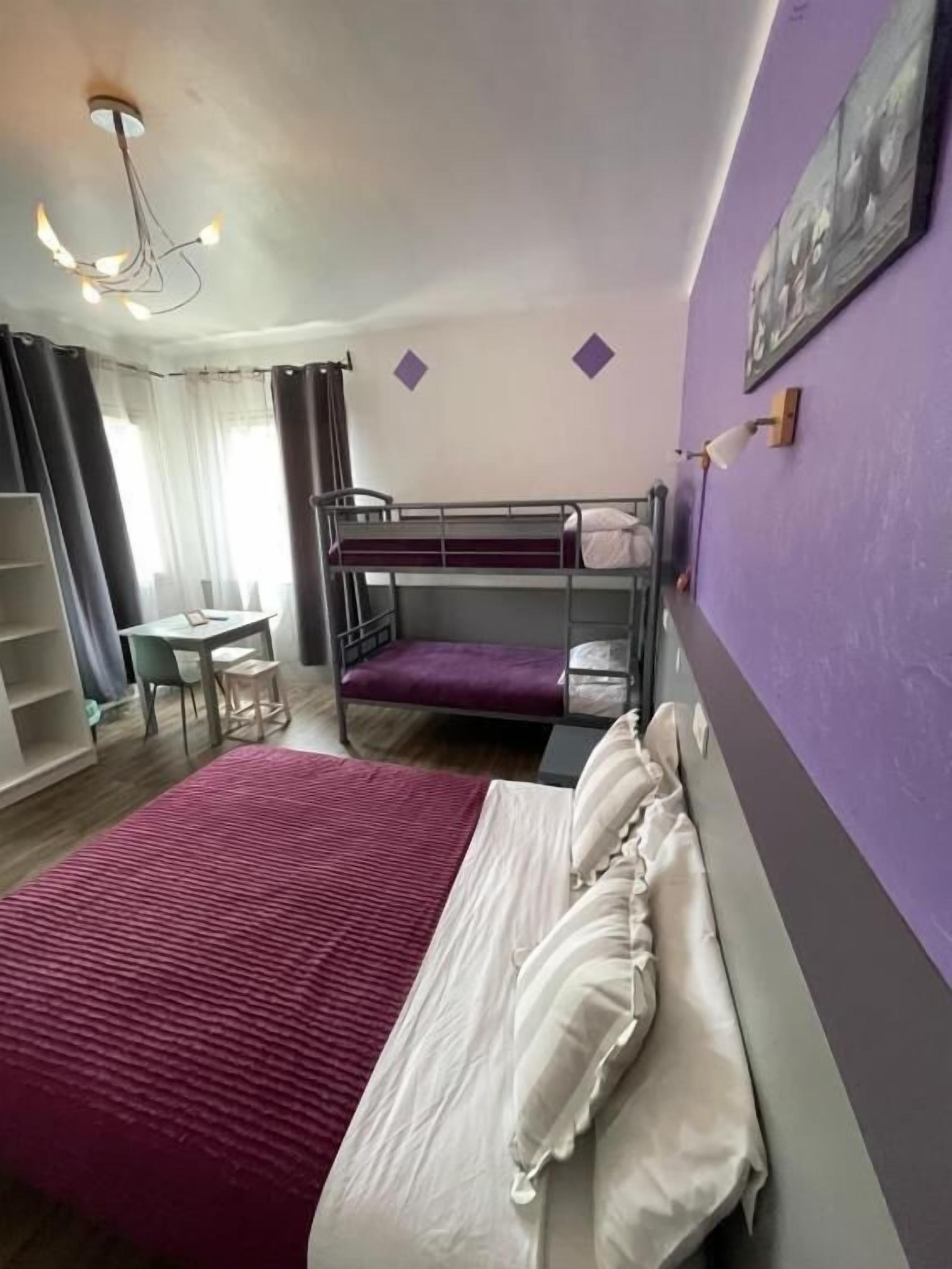 Una habitación con literas, un escritorio, una silla y una cama con una colcha roja.
